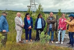 Grupa osób – przedstawiciele władz Powiatu Szamotulskiego i Uniwersytetu Przyrodniczego w Poznaniu – stojących na torfowisku przy urządzeniach pomiarowych.