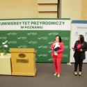 Oficjalne powitanie. Dwie kobiety na podium, przemawiające do publiczności, za nimi jest zielony ekran z napisem - Uniwersytet Przyrodniczy w Poznaniu