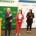 Trójka mówców na podium, a za nimi widnieje zielony baner - ekrann z napisem - Uniwersytet Przyrodniczy w Poznaniu