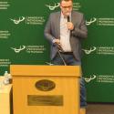 Mężczyzna na podium, wygłaszający przemówienie z poważną postawą, angażujący publiczność.