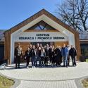 Zdjęcie grupowe studentów drugiego stopnia, II roku Gospodarki Przestrzennej z prof. UPP dr. hab. inż. Adamem Zydroniem oraz dr. inż. Cyprianem Chwiałkowskim przed budynkiem z panelami słonecznymi. Na budynku widoczny napis "Centrum Edukacji i Promocji Drewna"