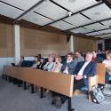 Zgromadzeni uczestnicy seminarium "ReBioClim" siedzą w audytorium Uniwersytetu Przyrodniczego w Poznaniu, słuchając prezentacji dotyczącej renaturyzacji cieków miejskich. Siedzą w rzędach, z których pierwsze zajmują starsze osoby, a z boku widać fragment drewnianej ściany. W oddali dostrzec można nagłówek "WYDZIAŁ INŻYNIERII ŚRODOWISKA I INŻYNIERII MECHANICZNEJ".